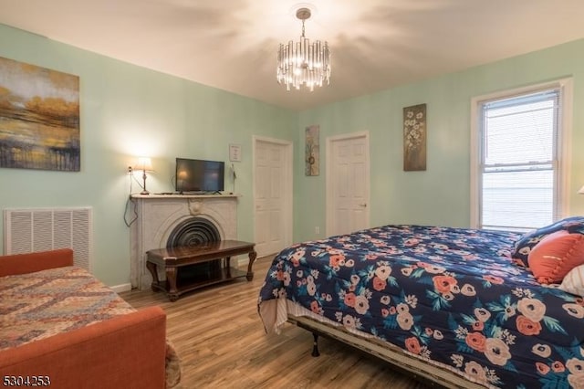 bedroom with a chandelier, visible vents, a fireplace, and wood finished floors