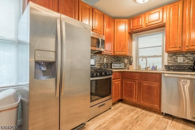 kitchen featuring light wood finished floors, stainless steel appliances, tasteful backsplash, a sink, and light stone countertops