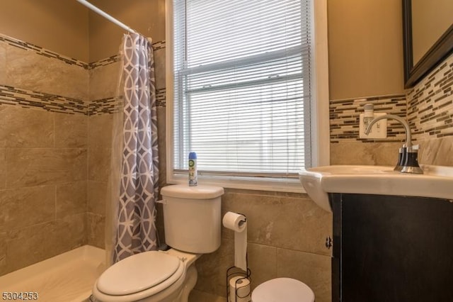 bathroom featuring tiled shower, vanity, toilet, and tile walls