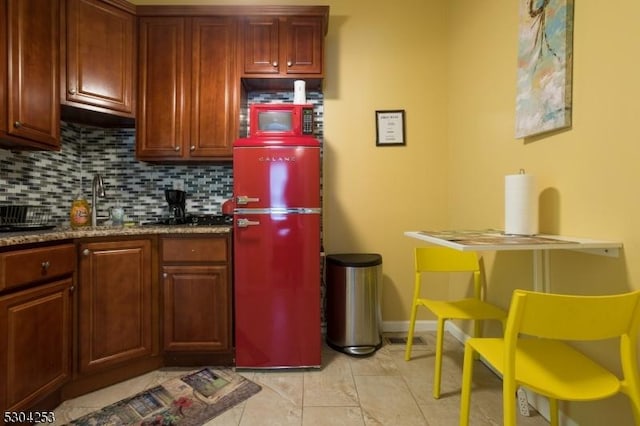 kitchen featuring white microwave, baseboards, decorative backsplash, and dark stone countertops