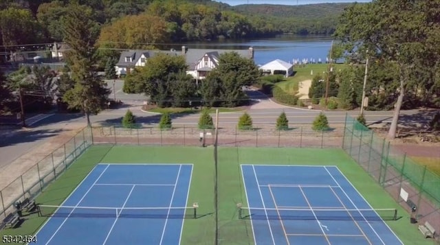 view of sport court with a forest view, a water view, and fence