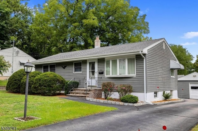 single story home featuring an outbuilding, a front yard, aphalt driveway, a chimney, and a detached garage