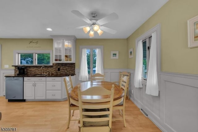 dining area with a ceiling fan, wainscoting, and light wood finished floors