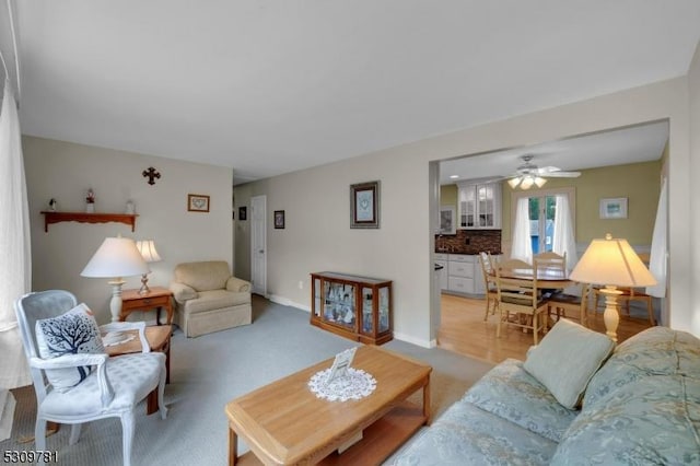 living room featuring baseboards, light colored carpet, and a ceiling fan