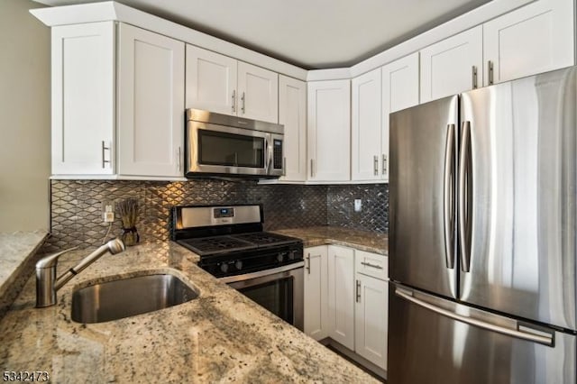 kitchen with appliances with stainless steel finishes, white cabinetry, a sink, and backsplash