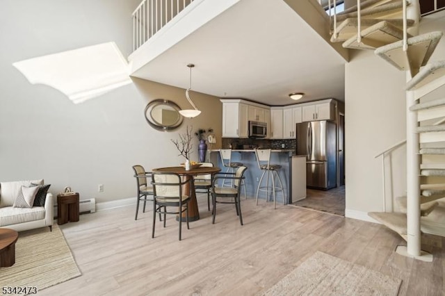 dining room with a baseboard radiator, stairway, a high ceiling, light wood-style flooring, and baseboards