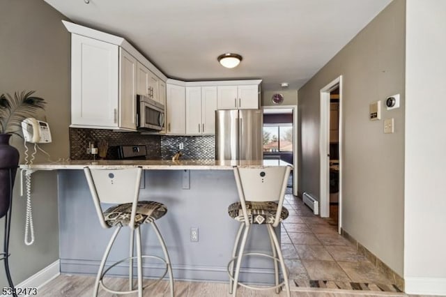 kitchen featuring a peninsula, white cabinetry, appliances with stainless steel finishes, and decorative backsplash