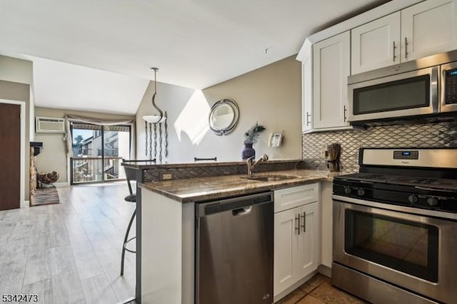 kitchen featuring a peninsula, a sink, appliances with stainless steel finishes, decorative backsplash, and a wall mounted air conditioner