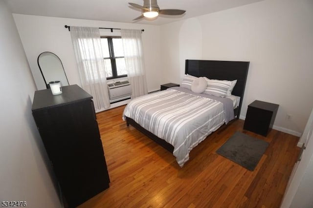 bedroom featuring baseboards, ceiling fan, wood finished floors, baseboard heating, and cooling unit