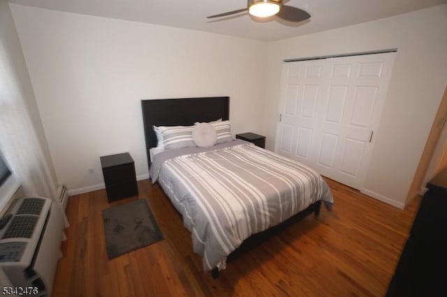 bedroom featuring a wall unit AC, wood finished floors, a ceiling fan, baseboards, and a closet