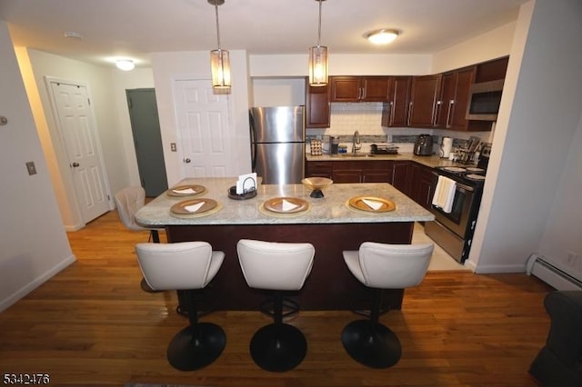 kitchen featuring decorative backsplash, decorative light fixtures, stainless steel appliances, light wood-style floors, and a sink