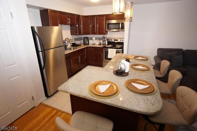 kitchen featuring a breakfast bar, backsplash, appliances with stainless steel finishes, light wood-style floors, and a sink