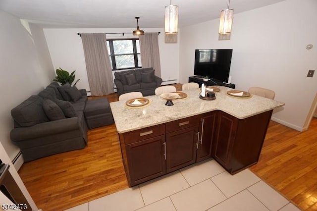 kitchen featuring decorative light fixtures, light wood-style flooring, baseboard heating, open floor plan, and light stone countertops