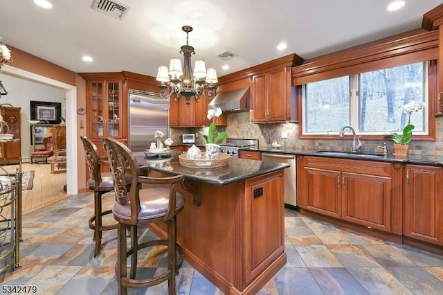 kitchen featuring visible vents, dark countertops, wall chimney exhaust hood, stainless steel appliances, and a sink