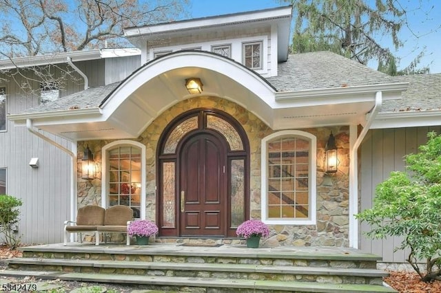 view of exterior entry with stone siding, a porch, and roof with shingles