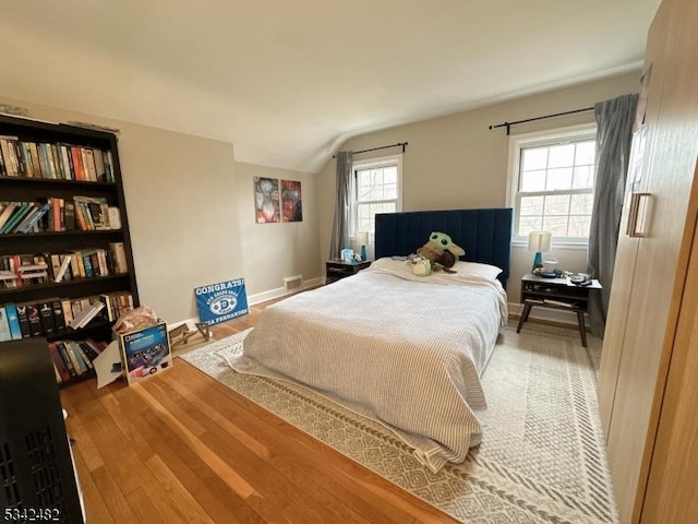 bedroom featuring lofted ceiling, visible vents, baseboards, and wood finished floors