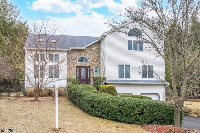 traditional home featuring stone siding, fence, a front lawn, and an attached garage