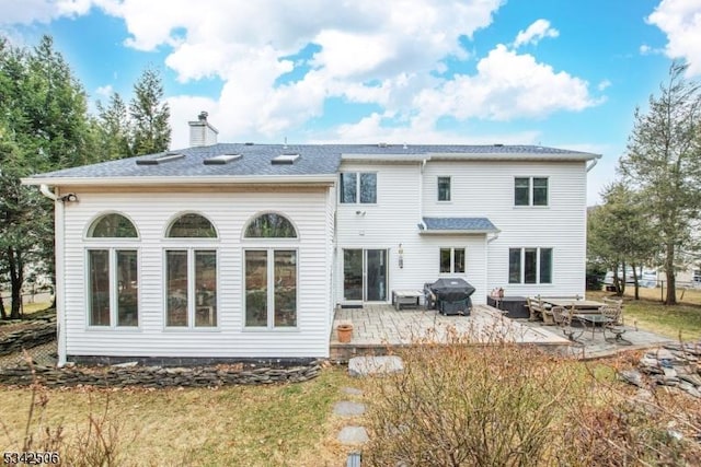 back of house with a shingled roof, a patio area, and a chimney