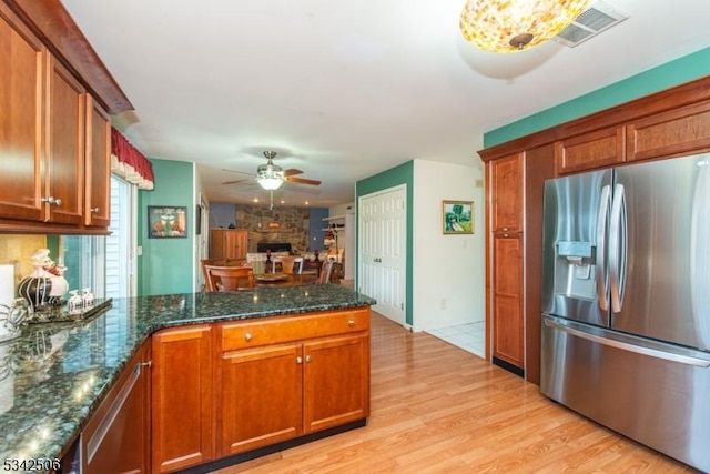 kitchen with ceiling fan, a large fireplace, a peninsula, visible vents, and stainless steel refrigerator with ice dispenser