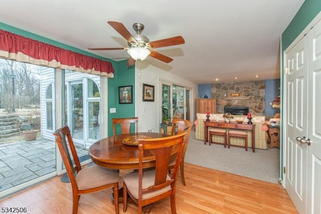 dining room featuring light wood-style floors, a fireplace, and a ceiling fan