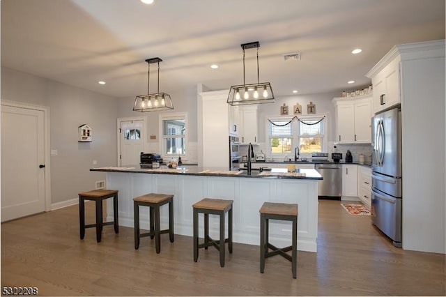 kitchen featuring a breakfast bar, stainless steel appliances, dark countertops, visible vents, and white cabinetry