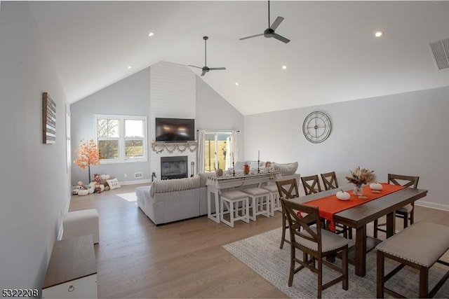 dining room with a fireplace, visible vents, light wood-style flooring, a ceiling fan, and high vaulted ceiling