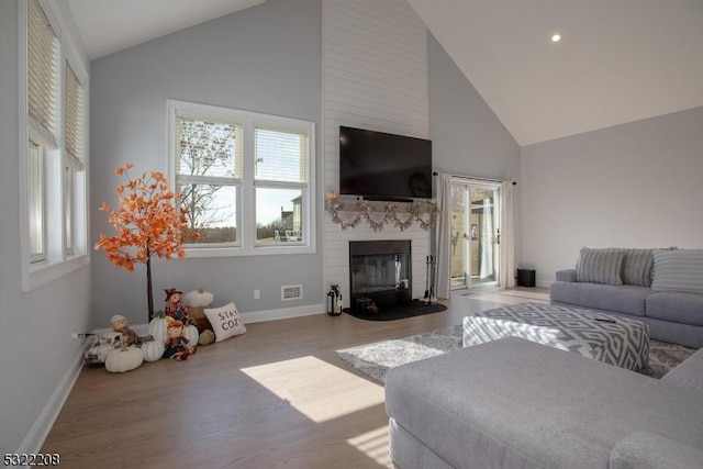 living room with visible vents, a large fireplace, wood finished floors, high vaulted ceiling, and baseboards