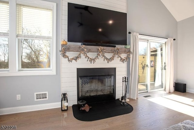 living room with baseboards, visible vents, wood finished floors, vaulted ceiling, and a fireplace