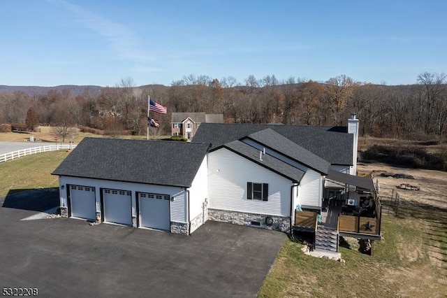 view of front of house featuring a detached garage, a shingled roof, a front yard, fence, and a wooded view