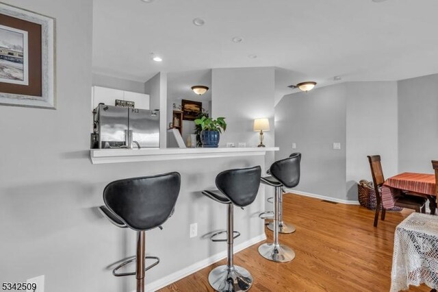 kitchen with a kitchen breakfast bar, baseboards, wood finished floors, and stainless steel fridge with ice dispenser