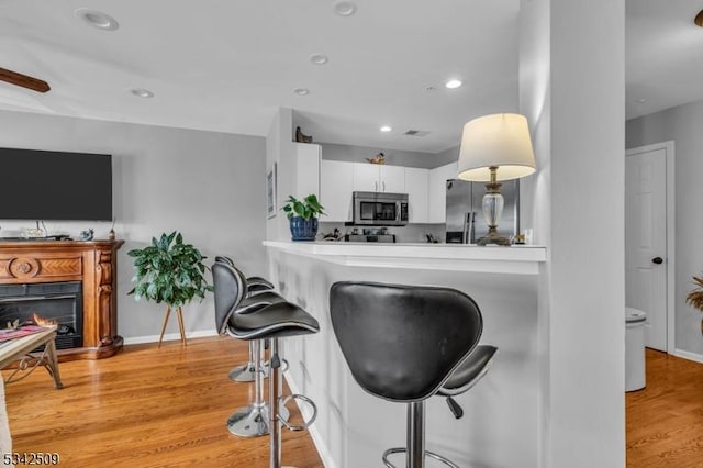 kitchen featuring stainless steel appliances, white cabinetry, a lit fireplace, light wood-type flooring, and a kitchen bar