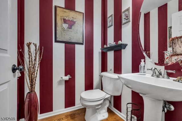 half bath with toilet, a sink, baseboards, and wood finished floors