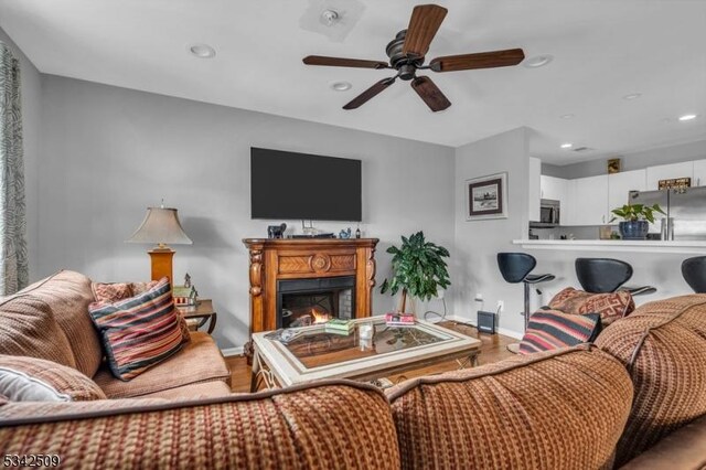 living room with recessed lighting, a lit fireplace, baseboards, and wood finished floors