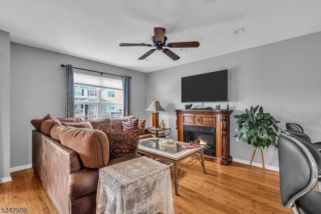 living area with light wood-type flooring, a glass covered fireplace, and baseboards