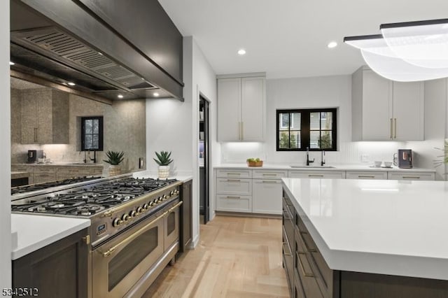 kitchen with range with two ovens, custom exhaust hood, light countertops, a sink, and recessed lighting