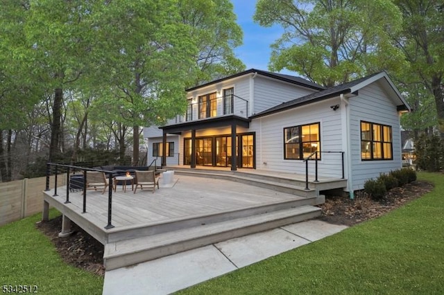 rear view of house with a balcony, an outdoor fire pit, a deck, and a yard