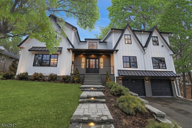 modern inspired farmhouse featuring aphalt driveway, an attached garage, board and batten siding, a standing seam roof, and a front lawn