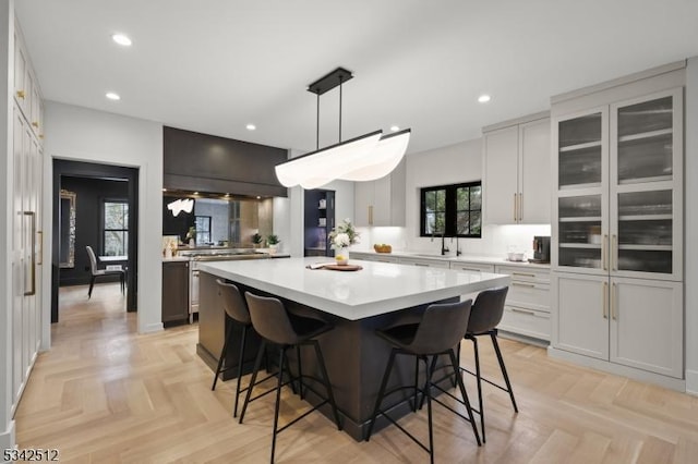 kitchen with a kitchen island, glass insert cabinets, a breakfast bar, light countertops, and recessed lighting