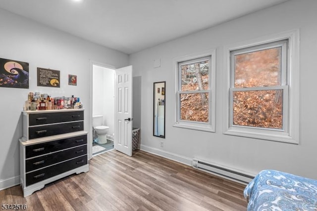 bedroom featuring a baseboard heating unit, baseboards, wood finished floors, and ensuite bathroom