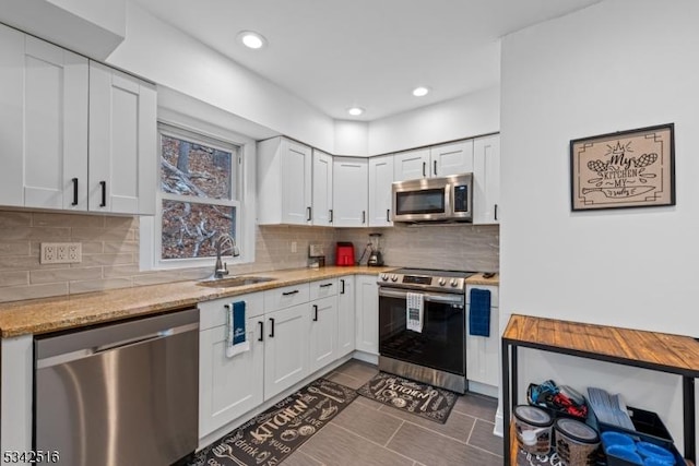 kitchen featuring light stone countertops, a sink, stainless steel appliances, white cabinets, and tasteful backsplash