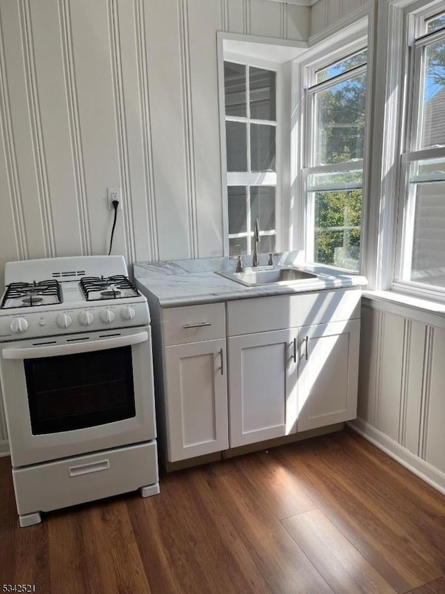 kitchen with white cabinets, dark wood-style floors, light stone countertops, white gas stove, and a sink