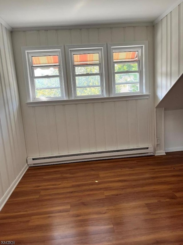 unfurnished room featuring a baseboard heating unit, a wealth of natural light, baseboards, and wood finished floors