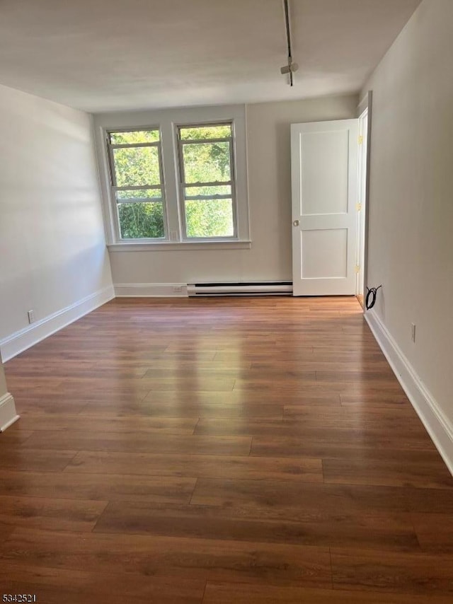 empty room with a baseboard heating unit, wood finished floors, and baseboards