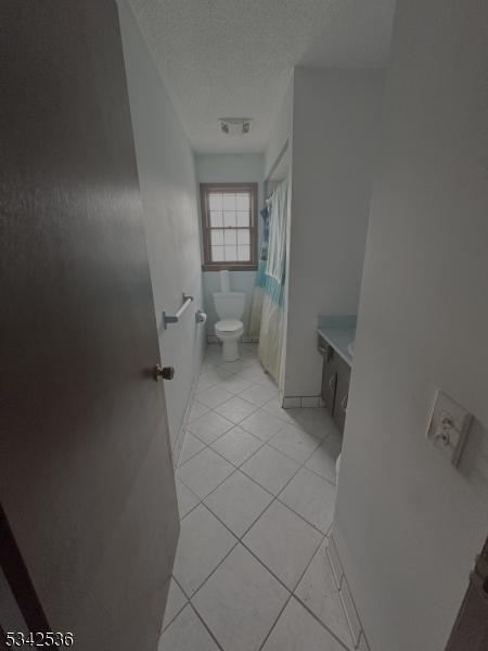 full bathroom with toilet, a shower with shower curtain, vanity, tile patterned floors, and a textured ceiling