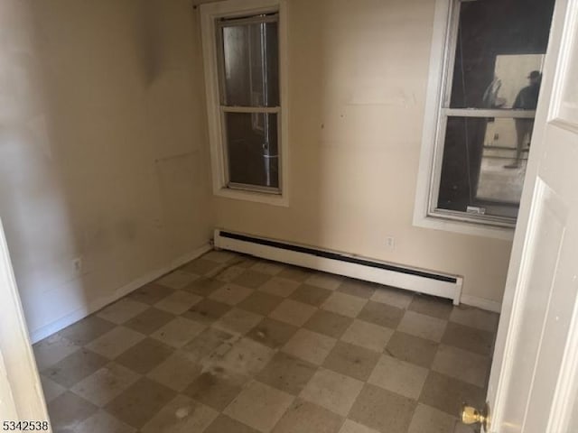 spare room featuring a baseboard heating unit, baseboards, and tile patterned floors