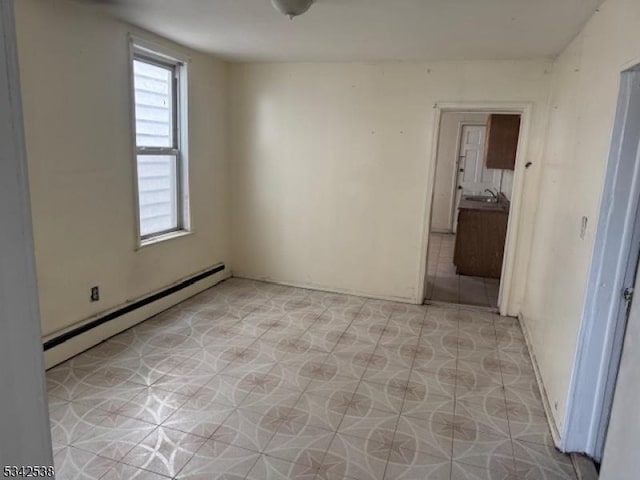 unfurnished room featuring baseboard heating and a sink