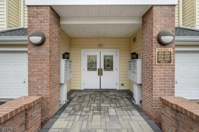 view of exterior entry with brick siding, a garage, french doors, and roof with shingles