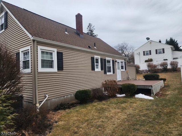 back of house with a deck, a yard, a shingled roof, and a chimney