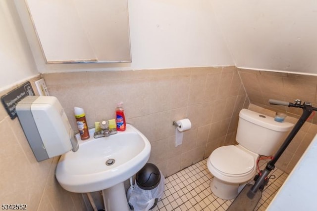 half bathroom featuring tile patterned flooring, toilet, a wainscoted wall, a sink, and tile walls