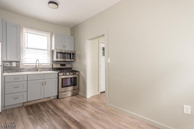 kitchen with baseboards, appliances with stainless steel finishes, gray cabinets, light wood-style floors, and a sink